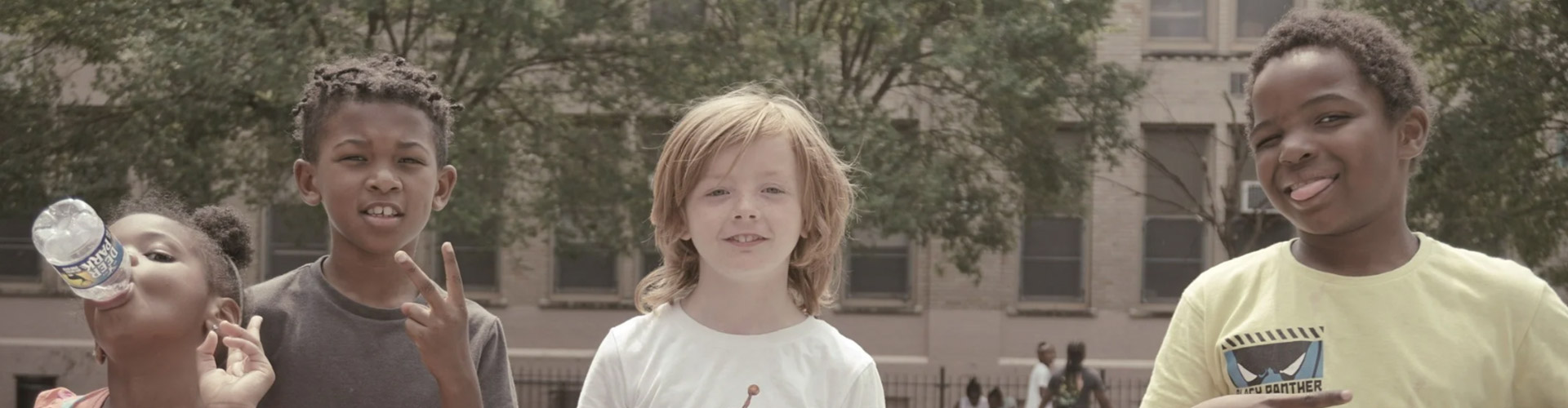 Three children enjoying a summer day, smiling and playing together in an outdoor community program.