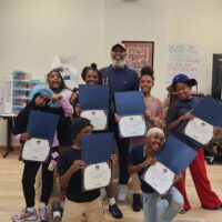 Group of smiling students holding certificates during the last day of Launch of Philadelphia's South West Peace Project with a mentor in the classroom.